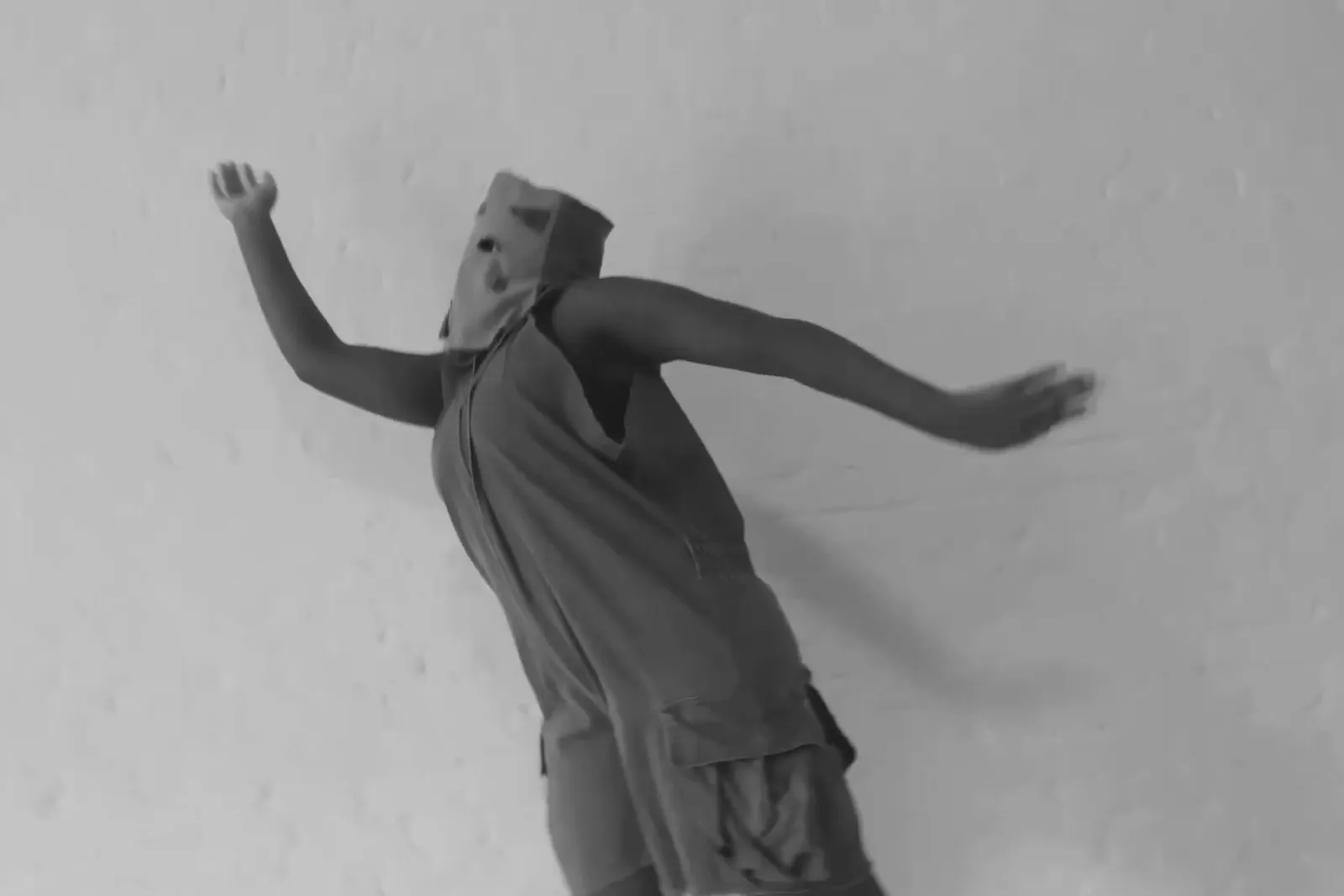 Artista com máscara de papel dança em cena em preto e branco
