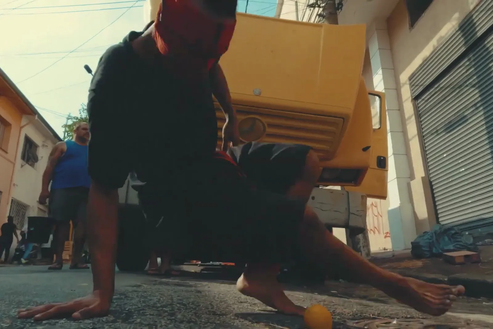 Artista mascarada dança no asfalto diante de um caminhão amarelo